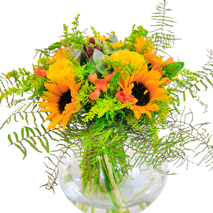 The impression left by this bouquet is unmistakably bright-a harmonious display of sunflowers and garden roses arranged in the local Harrow on the Hill tradition. Each sunflower is framed in a halo of yellow, their inky brown centers striking against the abundant greens. Close by, clusters of yellow roses open with sculptural perfection, petals curving inwards in tight, luxurious spirals. Among the blooms, shiny red Hypericum berries gleam, providing vivid accents that stand out like cherished treasures from a Harrow on the Hill flower market. The arrangement brims with greenery: feathery fern fronds extend gracefully, while light green filler with delicate yellow blossoms and sleek, vertical florets add height and softness, recalling the foliage seen on walks along Grove Hill. Eucalyptus leaves, tinged with blue-grey, peek through here and there, infusing the bouquet with a cool, wooded aroma. All elements converge in a clear, bowl-shaped vase-its perfect curve holding the stems in precise alignment, the water within reflecting the bouquet's lively palette. The scent of sunflowers and roses, gentle yet uplifting, carries memories of open-air markets and sun-washed gatherings on the Hill. This arrangement brings to mind special milestones-a birthday toast, an anniversary dinner, or simply greeting guests with a note of joy-crafted with the affection and expertise of a Harrow on the Hill florist.