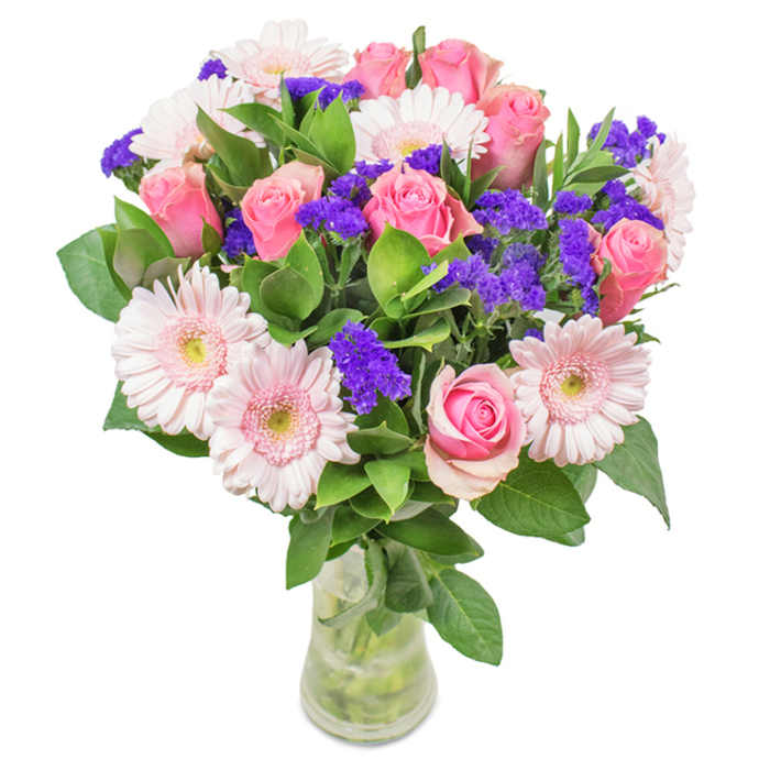 Prominently displayed in a clear glass vase against a pristine white backdrop, this floral composition is a standout piece from Harrow on the Hill's vibrant floristry scene. The centre is formed by 7-9 pink roses in varying stages of bloom-some with classic spiral shapes just beginning to open, setting the mood of understated romance. Five to seven pale pink gerbera daisies, known for their generous round heads and plethora of fine petals lightening to almost white at the core, enhance the soft play of colour, their shape recalling freshly planted beds around The Grove. Bright pops of purple statice (or limonium) interweave among the pinks, providing a modern edge and visual intrigue. Standing out against the pinks, rich, dense greenery grounds the composition like the mature foliage of Harrow's historic parks. The transparent vase, stems, and fresh water visible, completes the sense of local freshness-yard-fresh and ready for fast delivery to any address from West Street to the Hill itself. Appropriate for birthdays, anniversaries, special days like Mother's Day, or as an elegant accent for offices and homes, this Harrow on the Hill arrangement speaks of joy, sincerity, and affectionate celebration.